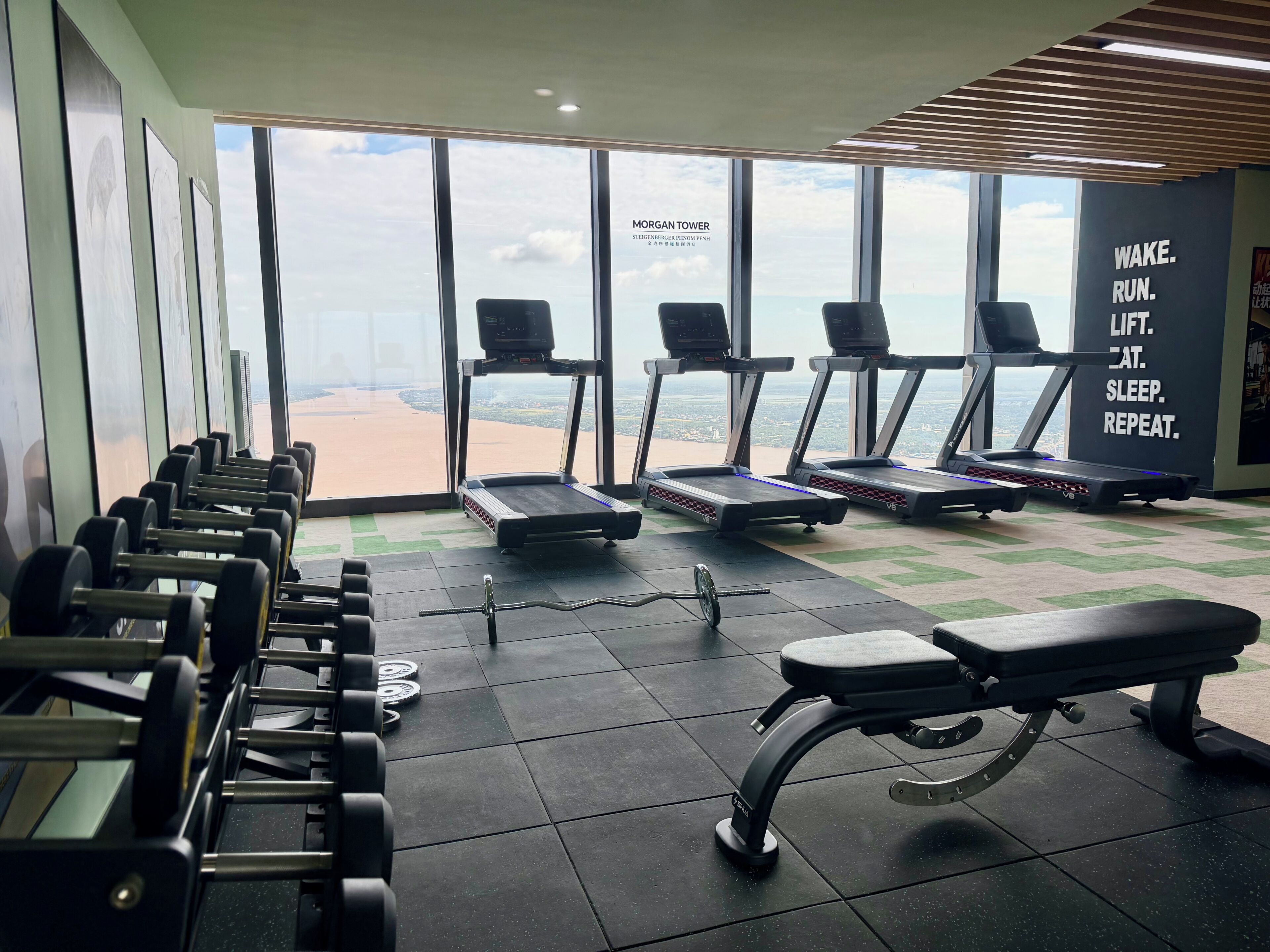 A gym with treadmills, dumbbells, and a bench.