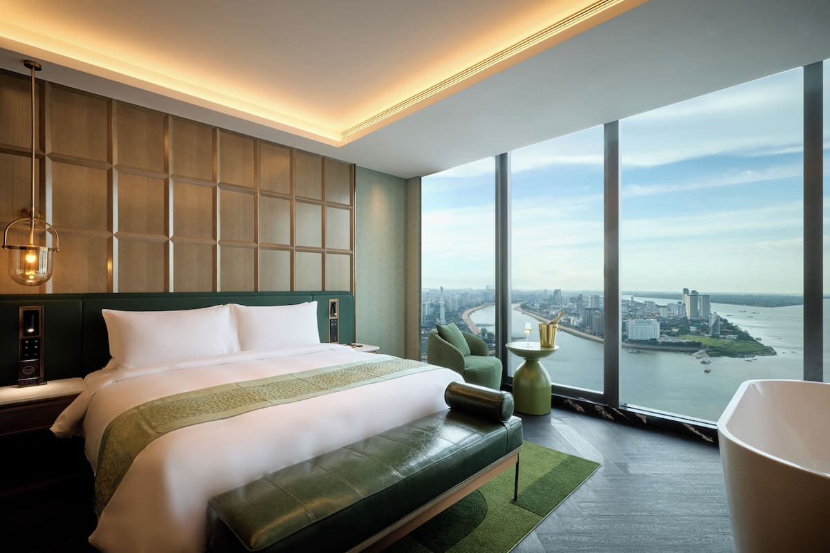 Una habitación de hotel moderna con una cama grande, vistas a la ciudad y al río, y una pared de acento verde.