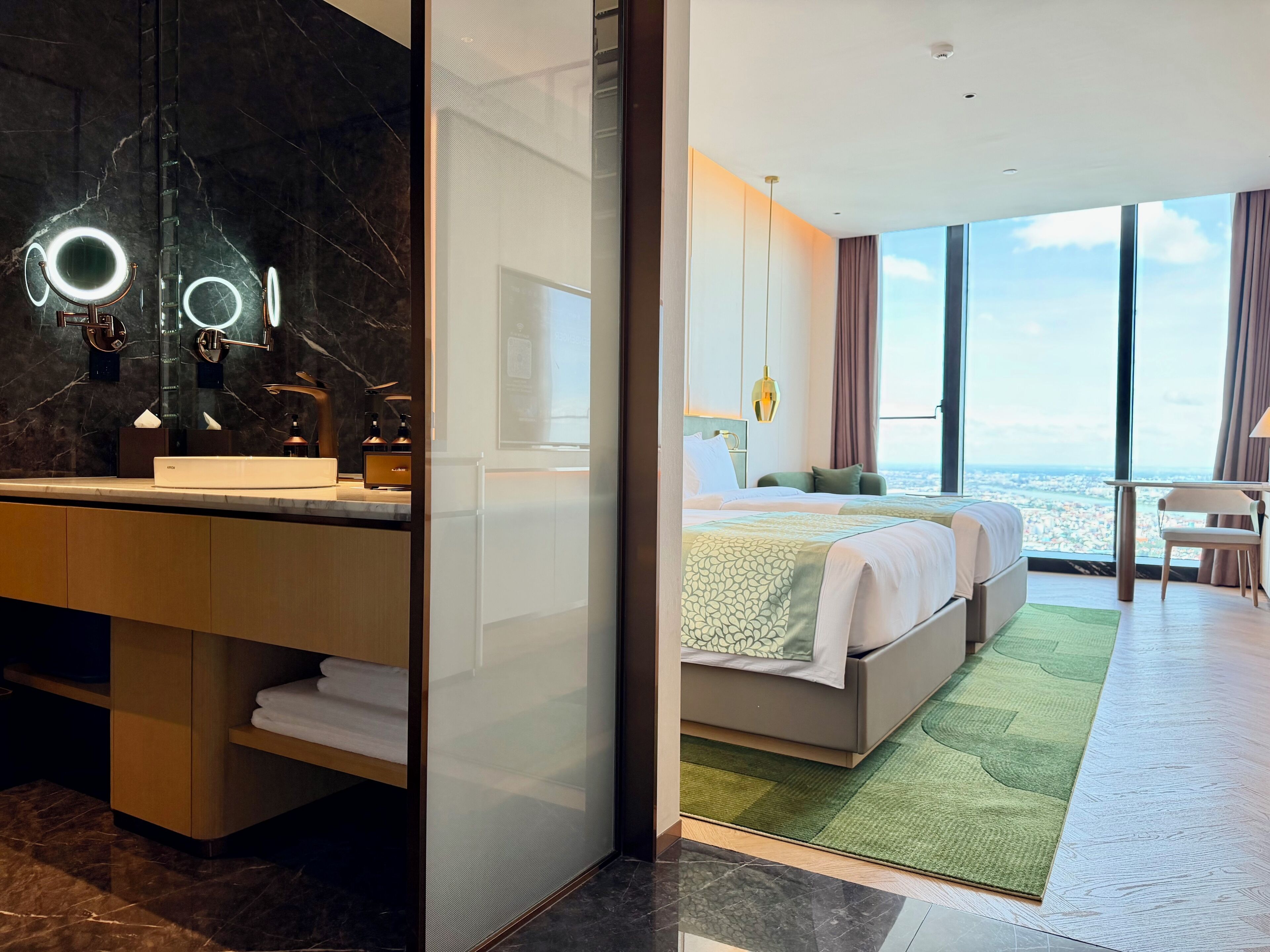 A modern hotel room with a bathroom vanity, a large mirror, a bed with a view, and a balcony.