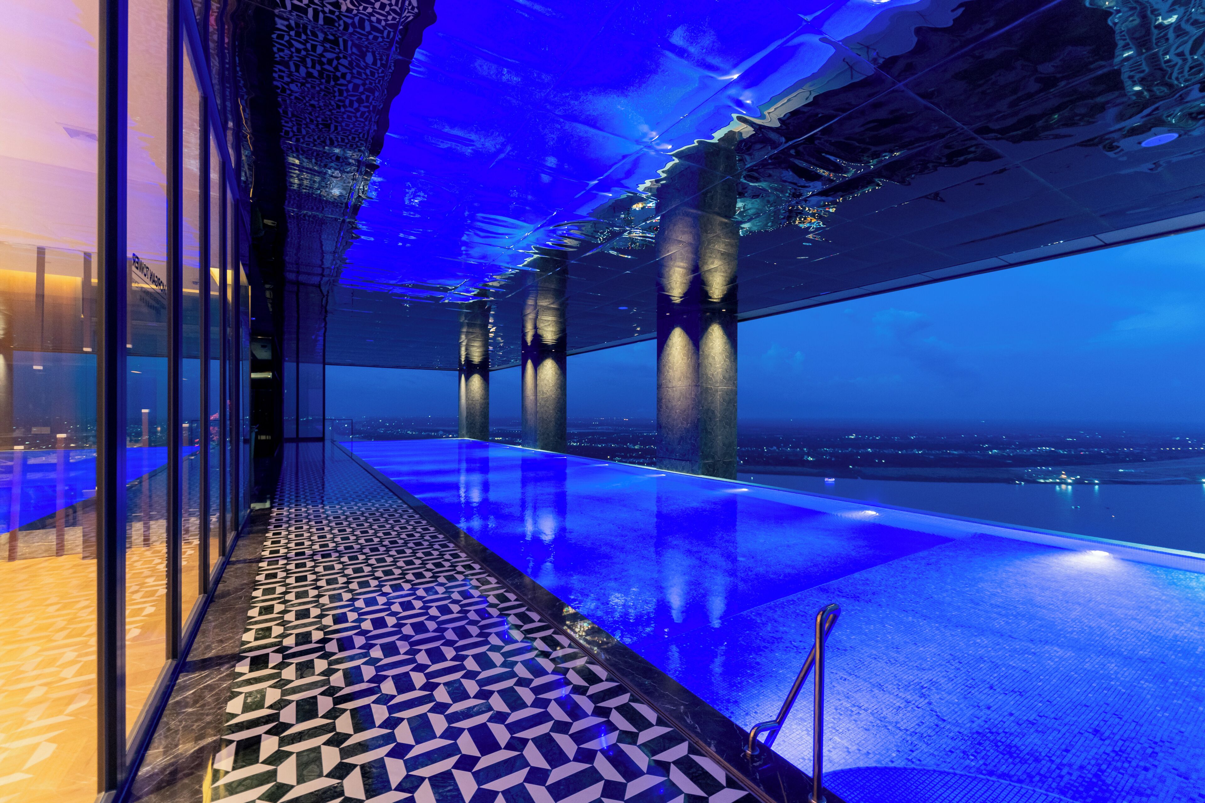 An infinity pool with a glass floor, a patterned floor design, and a city view.