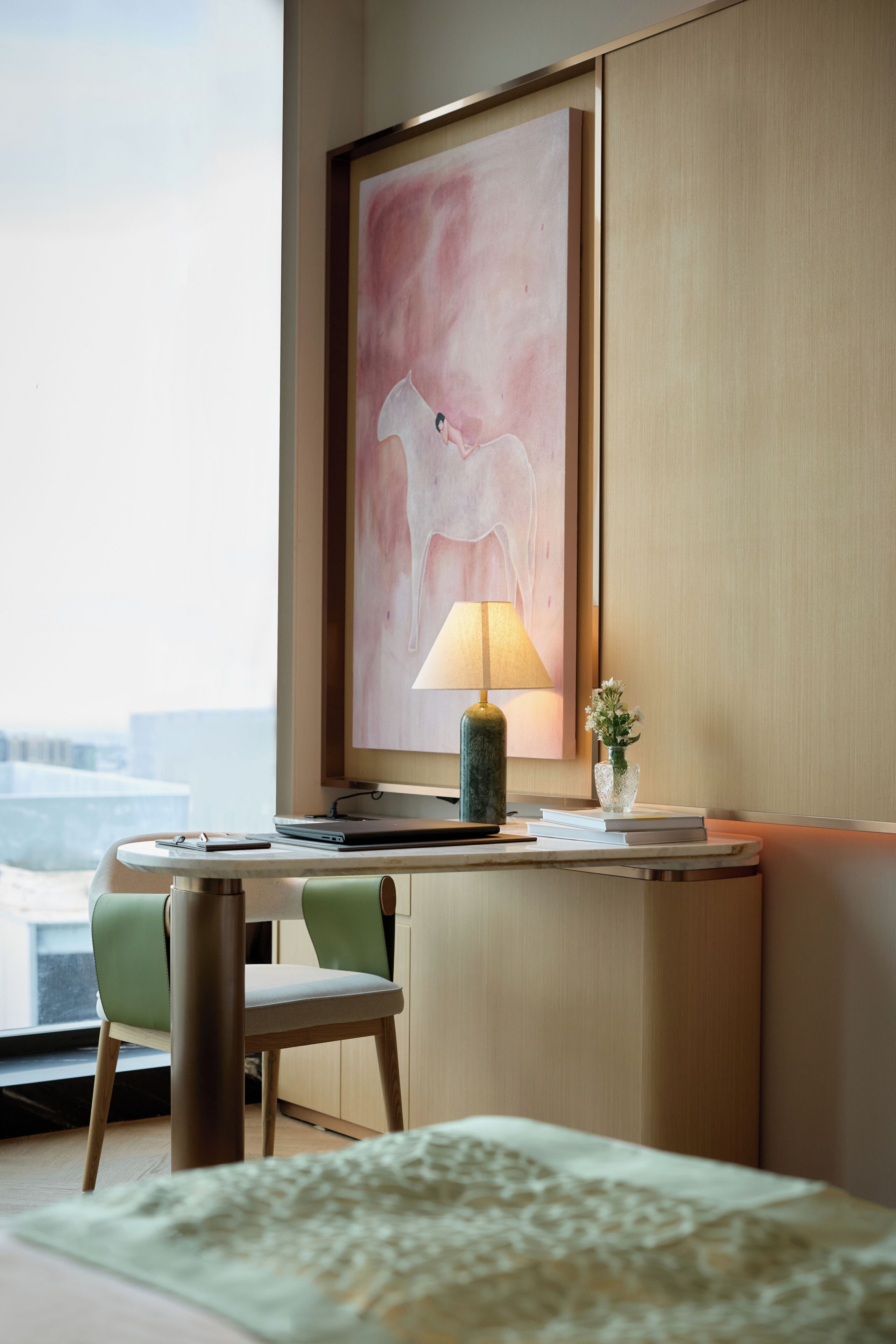Habitación de hotel con escritorio, lámpara, una obra de arte enmarcada, una planta pequeña y una cama con colcha estampada.