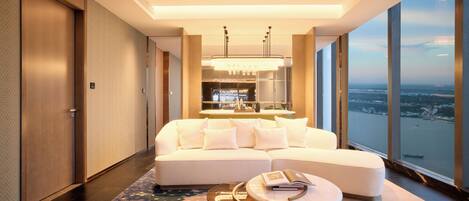 A modern hotel room with a large window, a sofa, a round coffee table, and a view of a cityscape.