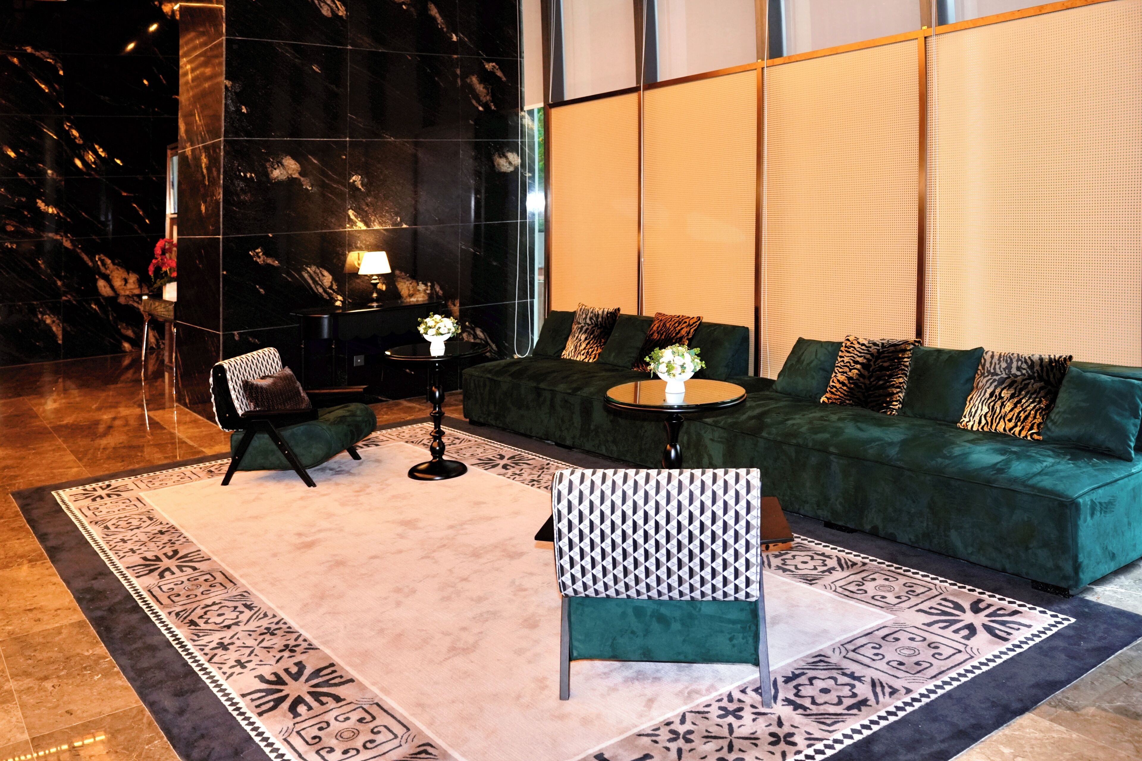 A modern lobby with a green sofa, patterned armchair, and a small round table with a lamp.
