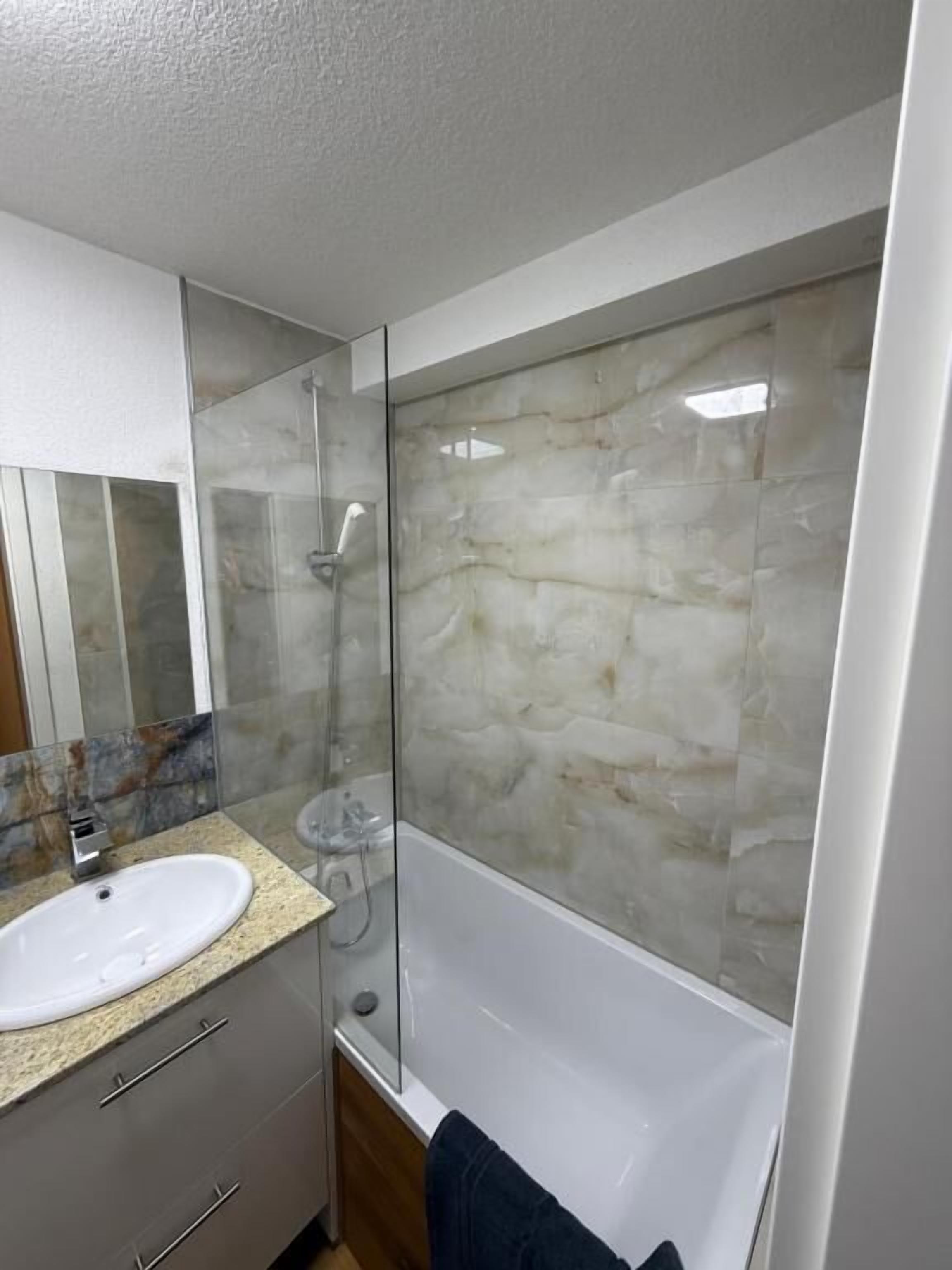 A bathroom with a white sink, a glass shower enclosure, and a marble wall.