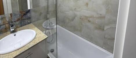A bathroom with a white sink, a glass shower enclosure, and a marble wall.