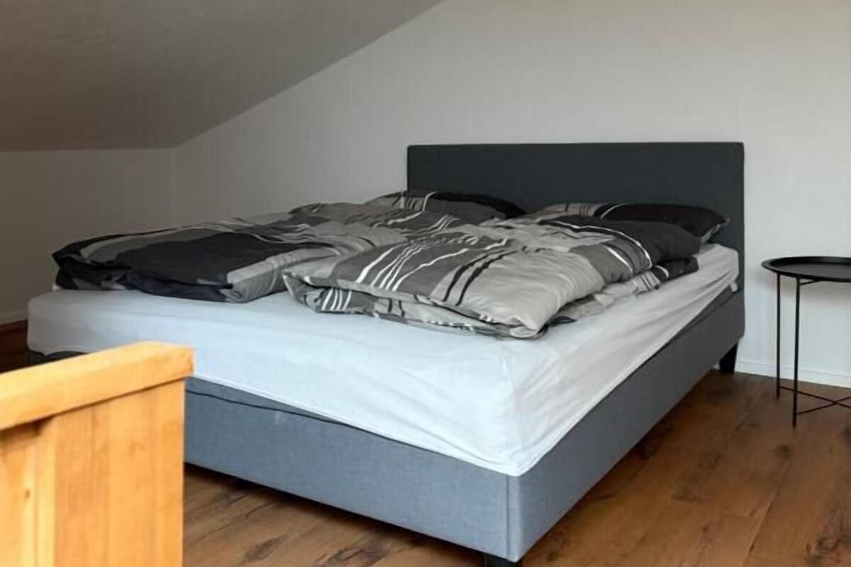 A bedroom with a bed, a small table, and a wooden chair.