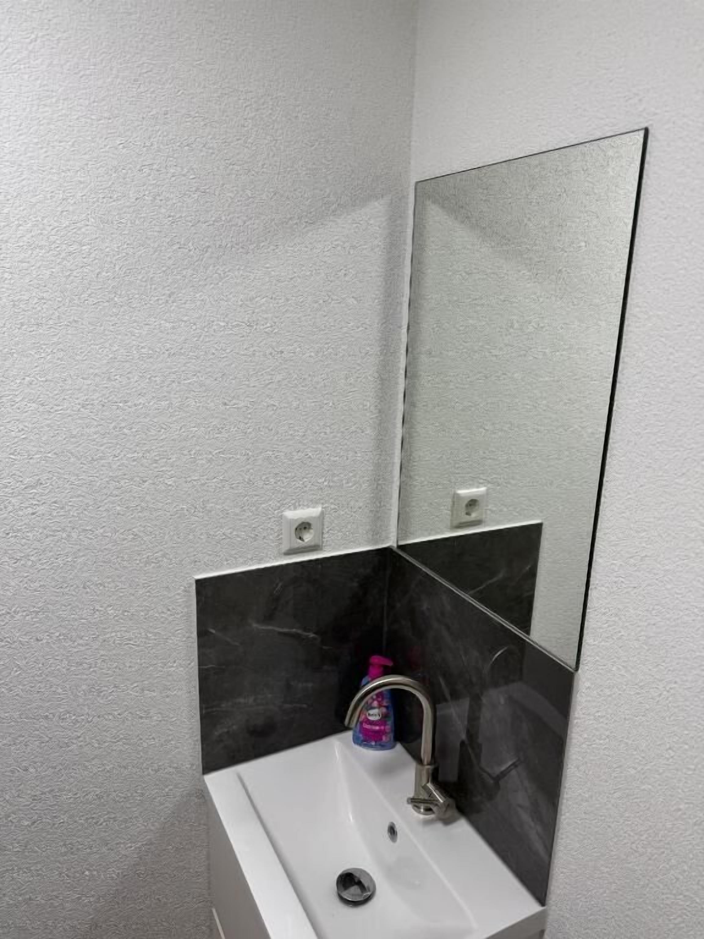 Ein Badezimmer mit einem weißen Waschbecken, einer schwarzen Marmor-Spritzschutzleiste und einem Spiegel.