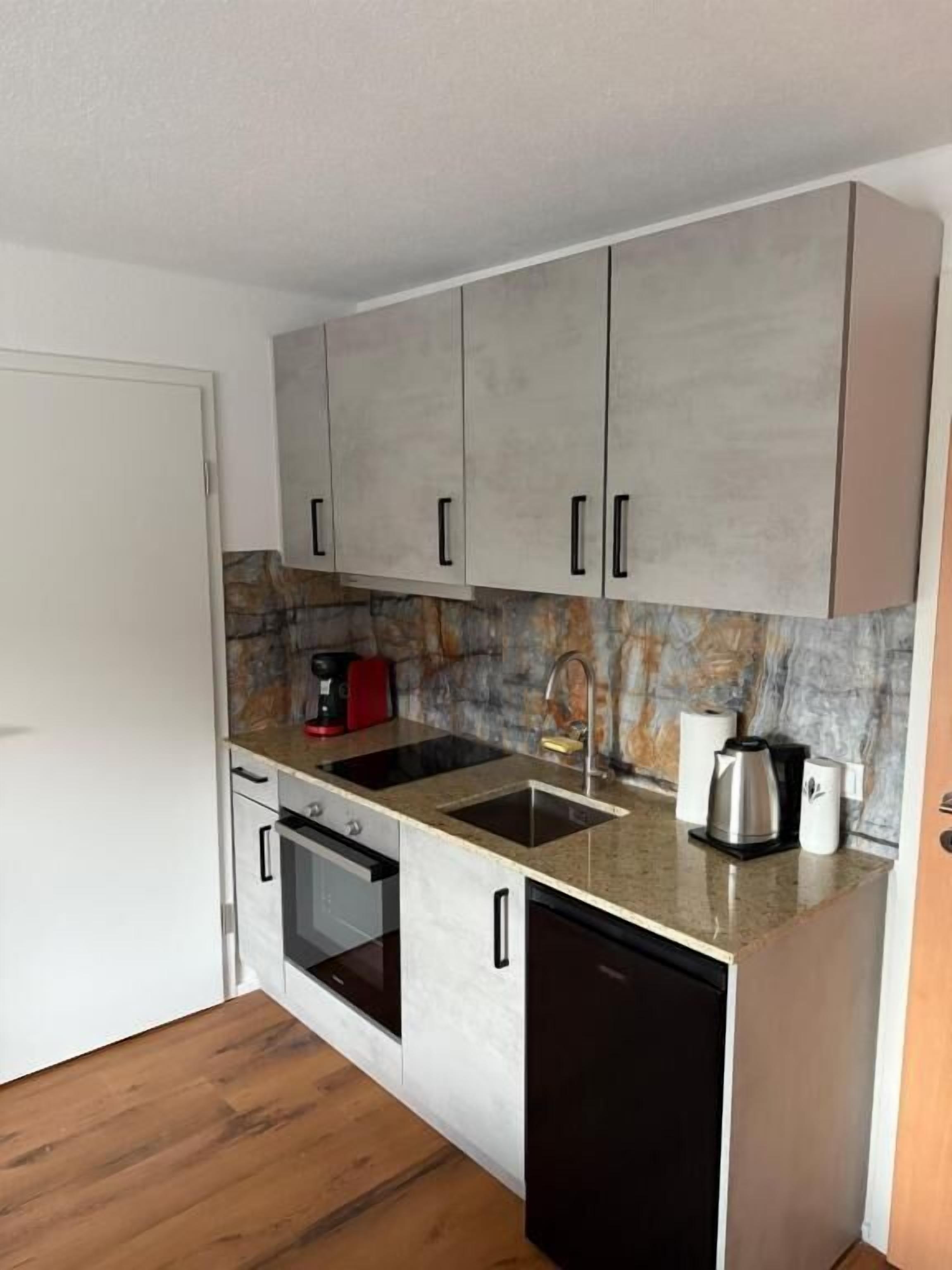 A compact kitchen with white cabinets, a black dishwasher, a built-in oven, and a granite countertop.