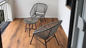 A balcony with two chairs and a small table, wooden flooring, and a white wall.