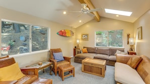 A cozy living room with a ceiling fan, large windows, a brown leather sofa, a wooden coffee table, and a wooden chair. - Near Beaches & Boat Launches! Lake Almanor Getaway (Lake Almanor)