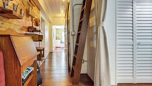 A narrow hallway with wooden shelves, a red chair, and a white door. - Walk to Southernmost Point! Conch Cottage w/ Patio (Key West)