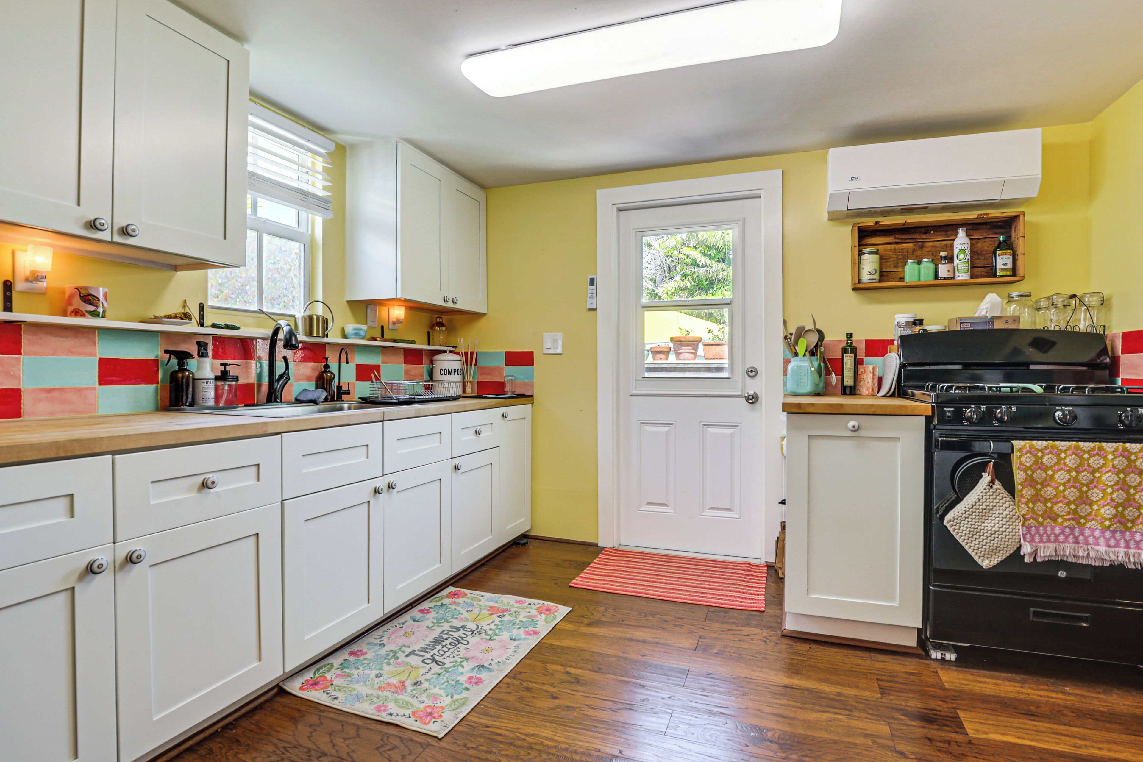 A kitchen with white cabinets, a wooden countertop, a stove, and a door with a window.