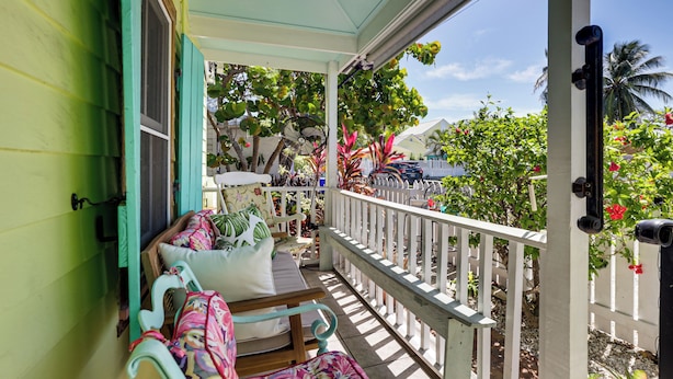 A porch with a white railing, a bench with floral cushions, and a fan. - Walk to Southernmost Point! Conch Cottage w/ Patio (Key West)