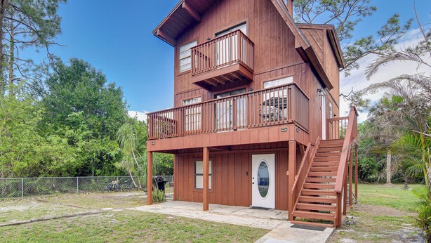 A two-story wooden house with a balcony, a front door, and a staircase leading to the upper level. - Lehigh Acres Home w/ Large Yard & Private Patio (Lehigh Acres)