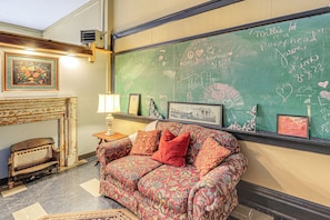 A cozy room with a patterned sofa, a framed picture, and a chalkboard with writings.