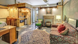 Een gezellige kamer met een houten eethoek, een groene schommelstoel, een kamerbreed tapijt en een open haard.