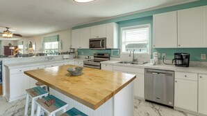 Een keuken met witte kasten, een houten eiland, een magnetron, een oven, een vaatwasser en een raam met jaloezieën.