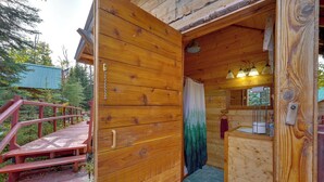 Een houten chalet met een houten trap naar een terras, een badkamer met douchegordijn en een klein wastafeltje.
