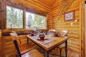 A wooden cabin interior with a dining table set for four, two windows, and a framed picture on the wall. - 3-Cabin Base w/ Lake Access: Dogs Welcome! (Soldotna)