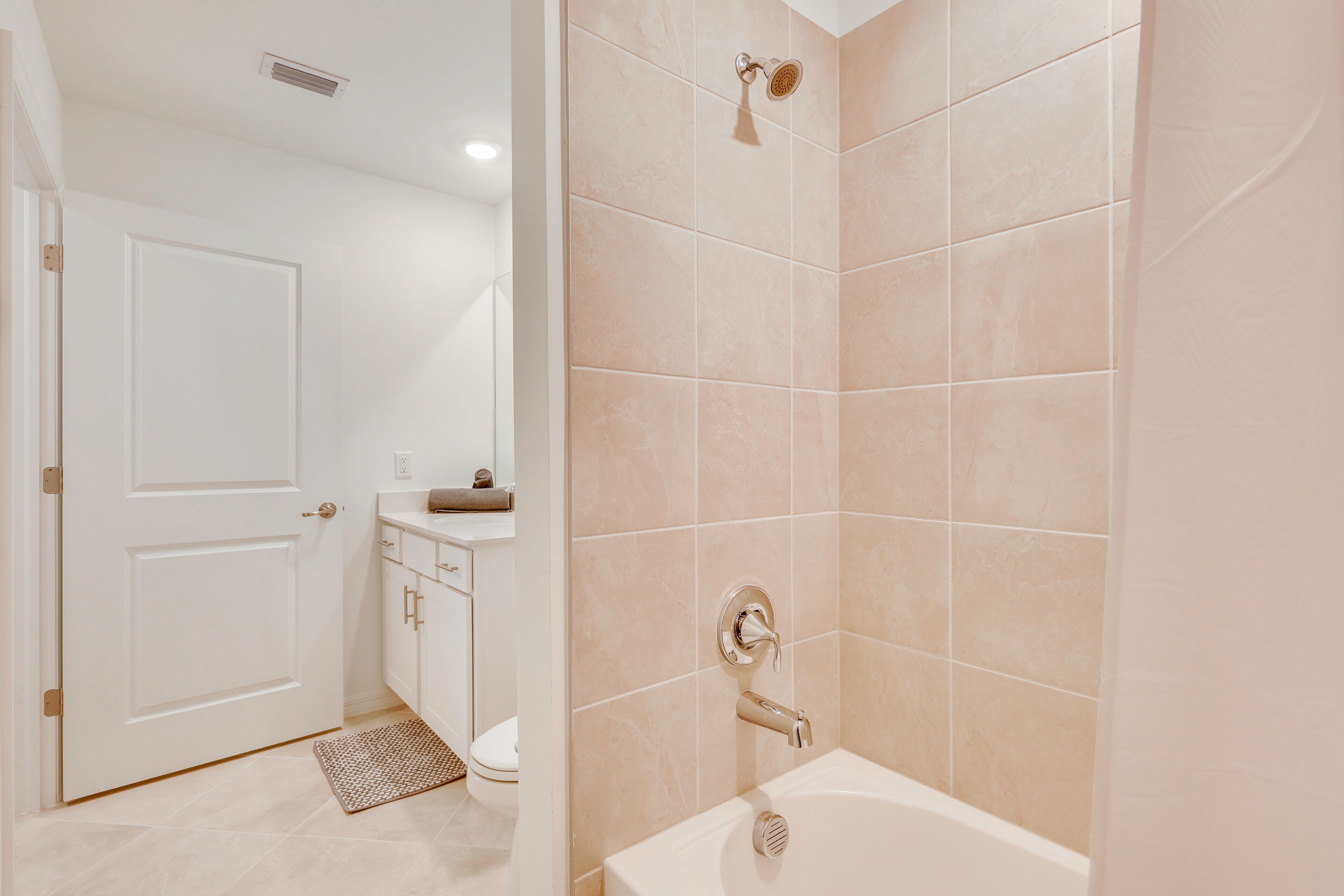 Un baño con azulejos color beige, una puerta blanca, un lavabo y una bañera.