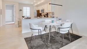 Een moderne keuken met witte kasten, een centraal eiland en een eethoek met witte stoelen en een ronde tafel.