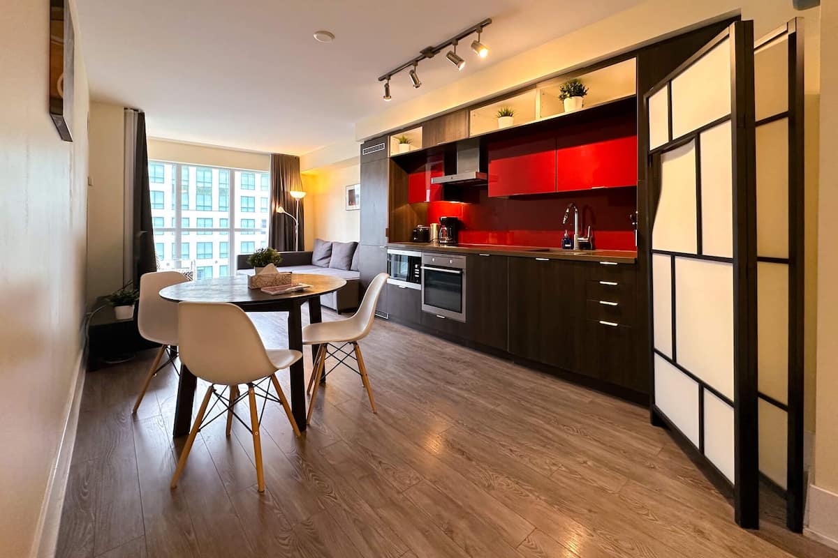 A modern kitchen with red cabinets, a dining area with a round table and chairs, and a view of a building through large windows.