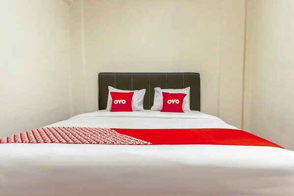 Habitación de hotel con cama, dos almohadas con la marca 'OYO' y una colcha con estampado rojo y blanco.