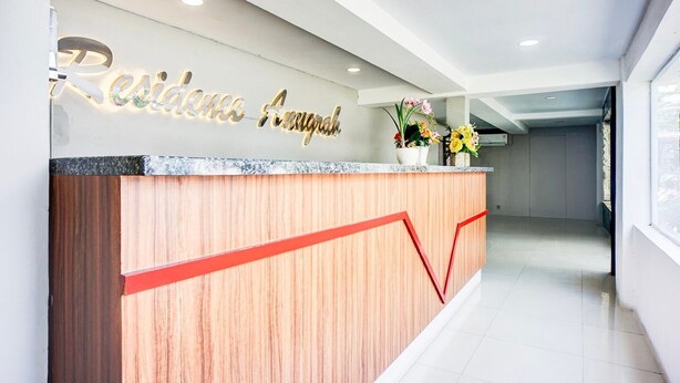 A reception desk with a wooden finish and a red accent line, a wall-mounted sign with illuminated letters, and a potted plant with yellow flowers. - Luxury Deluxe DBL Retreat W/ Free WiFi and Parking (Medan)