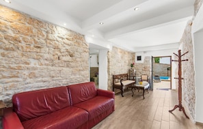 Ein geräumiger Raum mit einer Steinwand, einem roten Ledersofa, einem Holzmantelständer und Blick auf einen Außenbereich mit einem Pool.