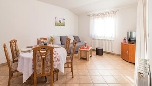 En matplats med ett bord för fyra personer, en soffa, ett litet sidobord, ett element och en tv.