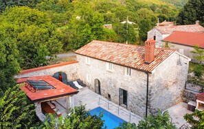 Un bâtiment en pierre avec un toit recouvert de tuiles rouges, une piscine et un patio aménagé avec du mobilier d’extérieur.