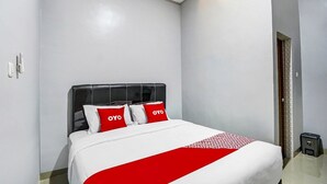 Une chambre d’hôtel avec un lit, des murs blancs et une couvre-lit rouge et blanche.