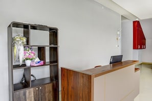 A reception desk with a wooden finish, a metal-framed shelving unit with a bouquet of flowers, and a red accent wall.