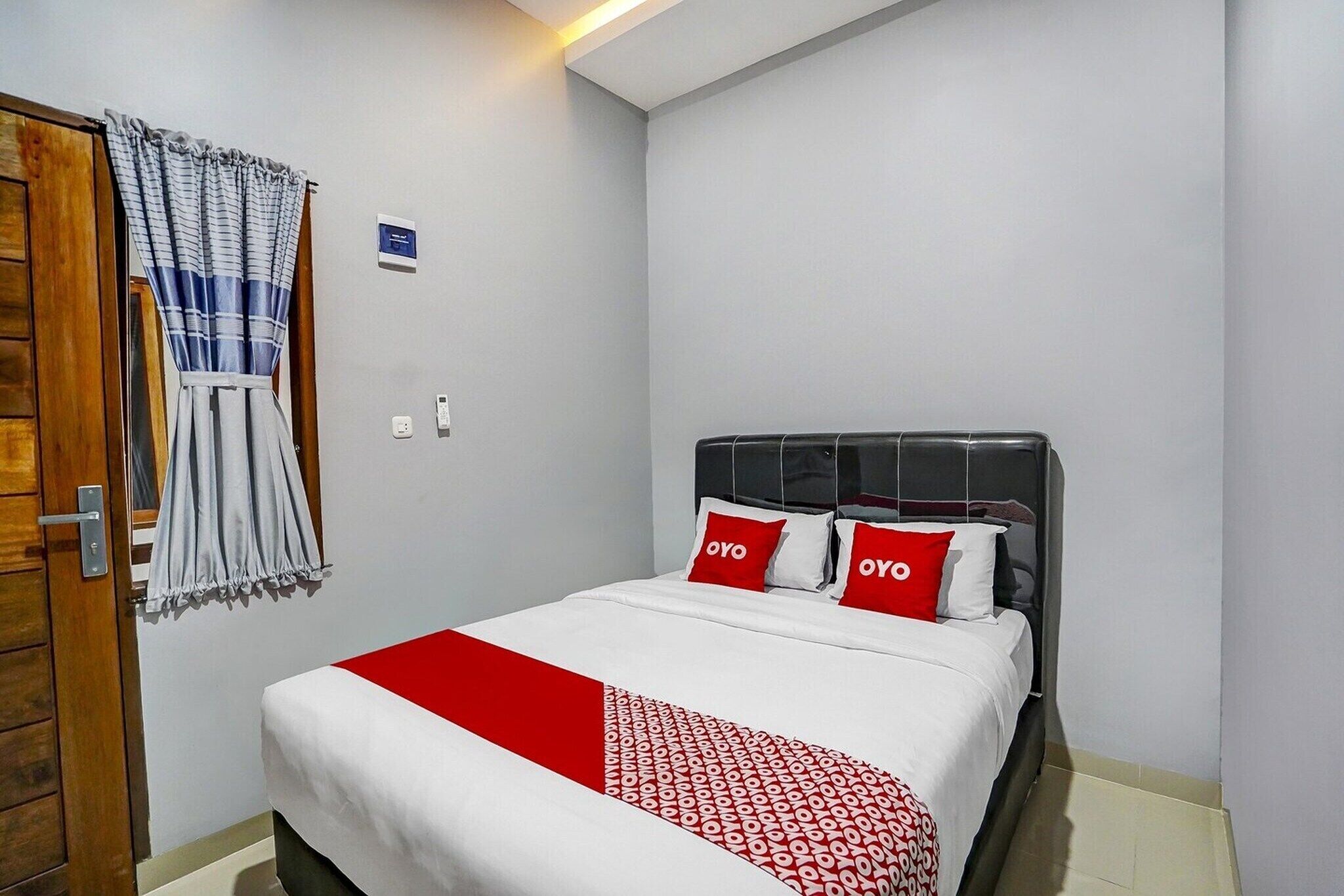Una habitación de hotel con una cama, una puerta de madera, una cortina y un termostato en la pared.