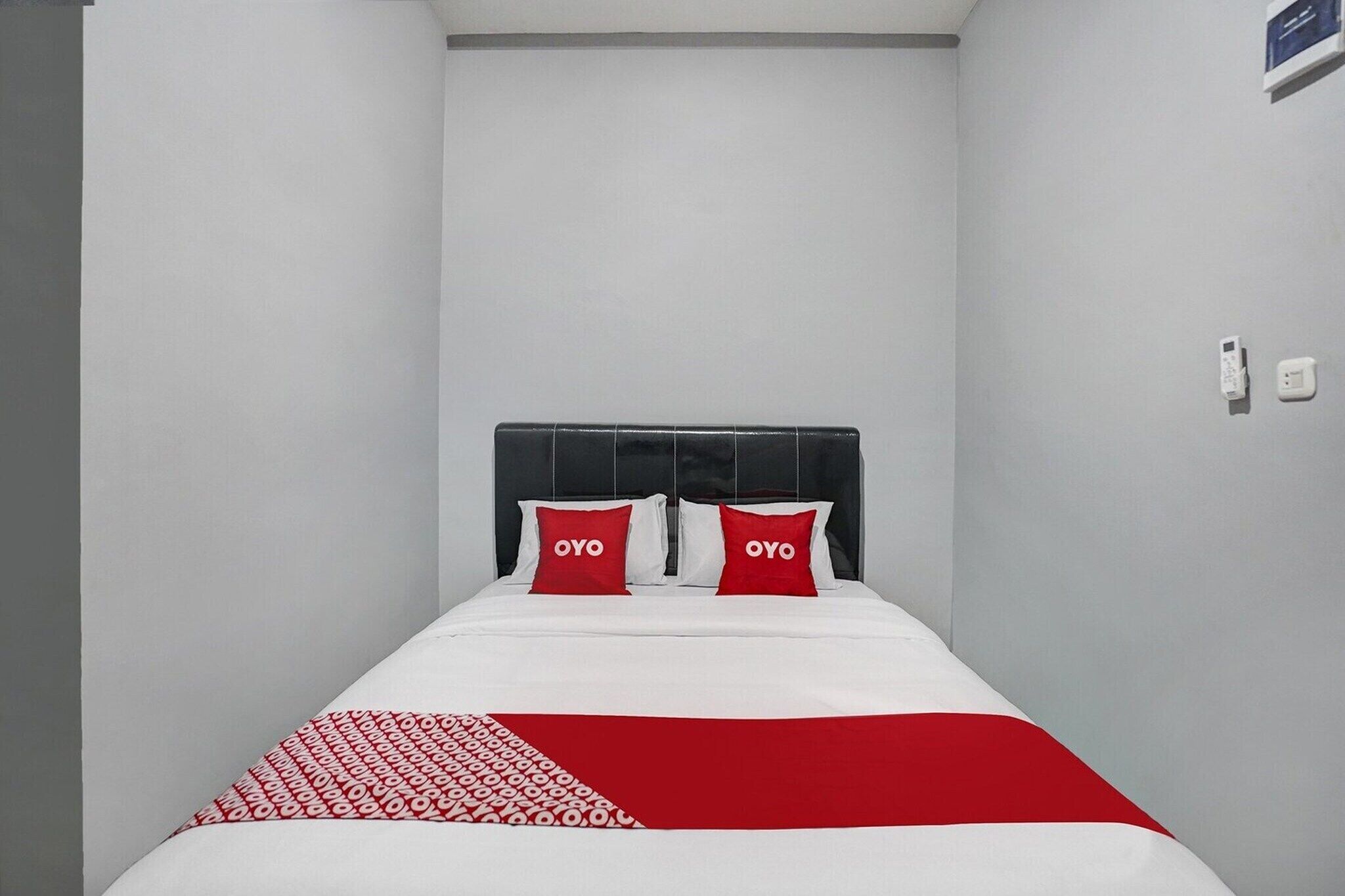 Ein Einzelbett mit schwarzem Kopfteil, zwei roten Kissen und einer weiß-rot gemusterten Bettdecke.