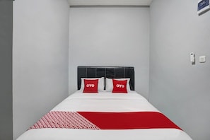 A single bed with a black headboard, two red pillows, and a white and red patterned bedspread.
