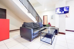 A modern living room with a black leather sofa, a glass coffee table, a staircase, and a flat-screen TV mounted on the wall. - Luxury Deluxe DBL Retreat W/ Free WiFi and Parking (Makassar)