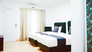 Un dormitorio con dos camas, una puerta blanca, una ventana con cortinas e un equipo de aire acondicionado.