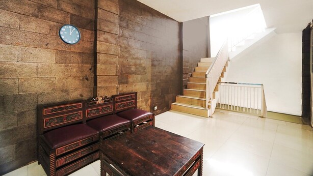 A room with a wooden bench, a table, a clock on the wall, and a staircase with a white railing.
