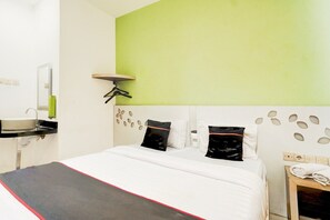 A hotel room with a bed, a bedside table, a mirror, a green accent wall, and a wall-mounted light fixture.
