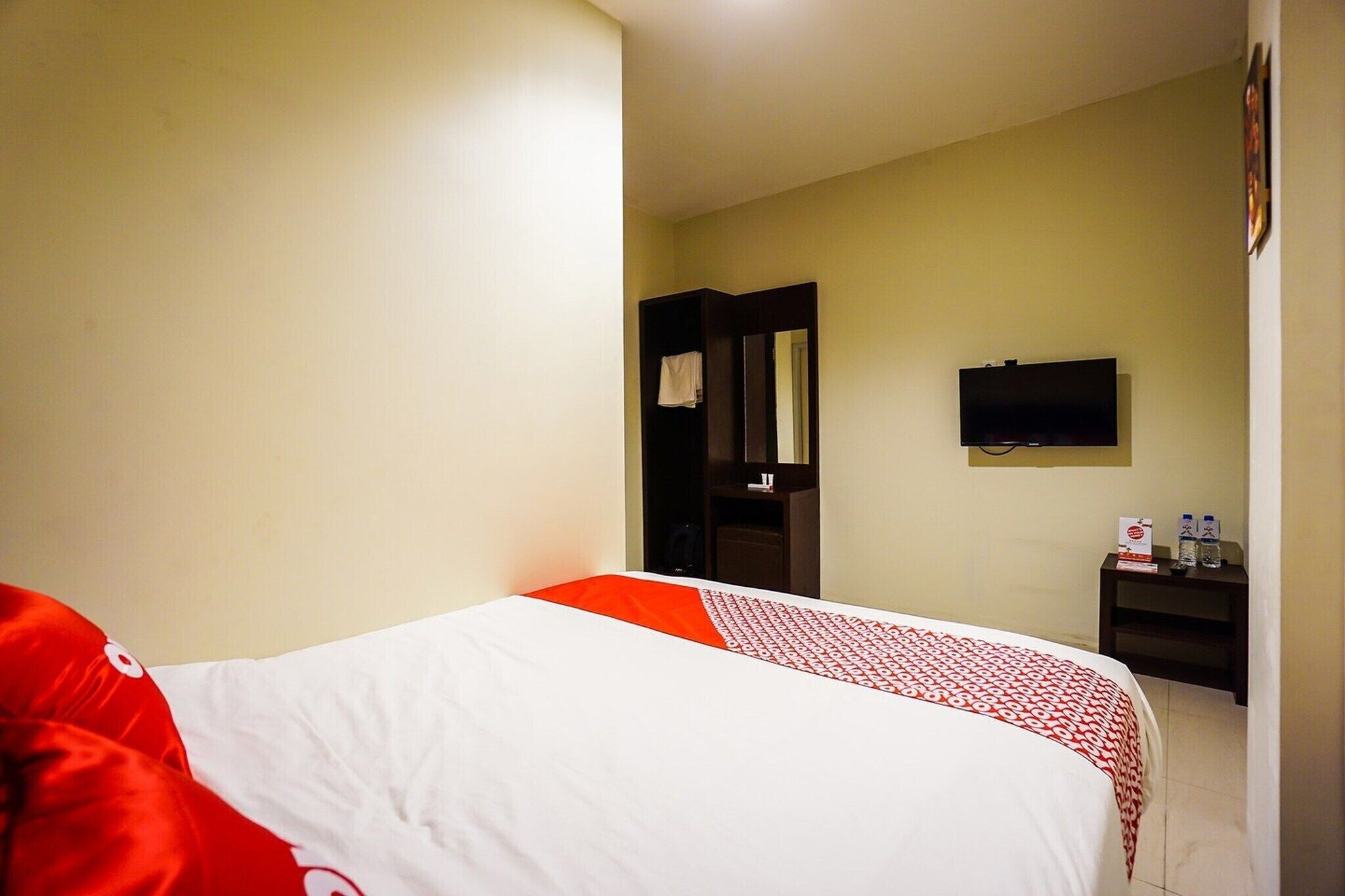 A hotel room with a bed, a television, a small table with bottles, and a door leading to another room.