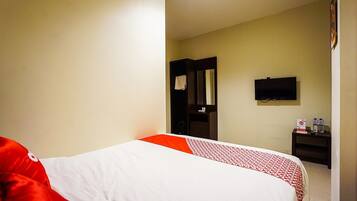 A hotel room with a bed, a television, a small table with bottles, and a door leading to another room.