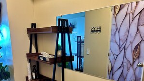 Una stanza con una sedia in legno, uno specchio con motivo a foglia e uno scaffale con articoli da bagno.