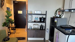Una cucina compatta con una macchina da caffè, bottiglie d'acqua, una cuociriso e un bollitore su uno scaffale.