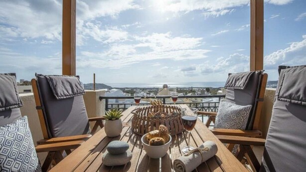 Eine Terrasse mit einer Holzpergola, zwei gepolsterten Stühlen, einem Tisch mit einem Brotkorb, einer Oliven-Schale und einem Weinglas.