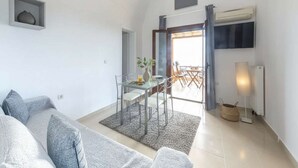 Ein modernes Wohnzimmer mit einer Couch, einem Esstisch mit Stühlen, einem Fernseher und einem großen Fenster.