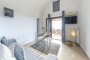 A modern living room with a sofa, a dining table with chairs, a TV, and a large window. - Apartment near Dinan Center (Megalochori)