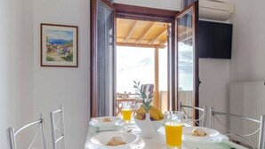 Ein Essbereich mit einem für das Frühstück gedeckten Tisch, einem Gemälde an der Wand und Blick durch eine offene Tür.