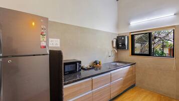 A kitchen with a stainless steel refrigerator, a microwave, wooden cabinets, a granite countertop, and a window with a view of trees.
