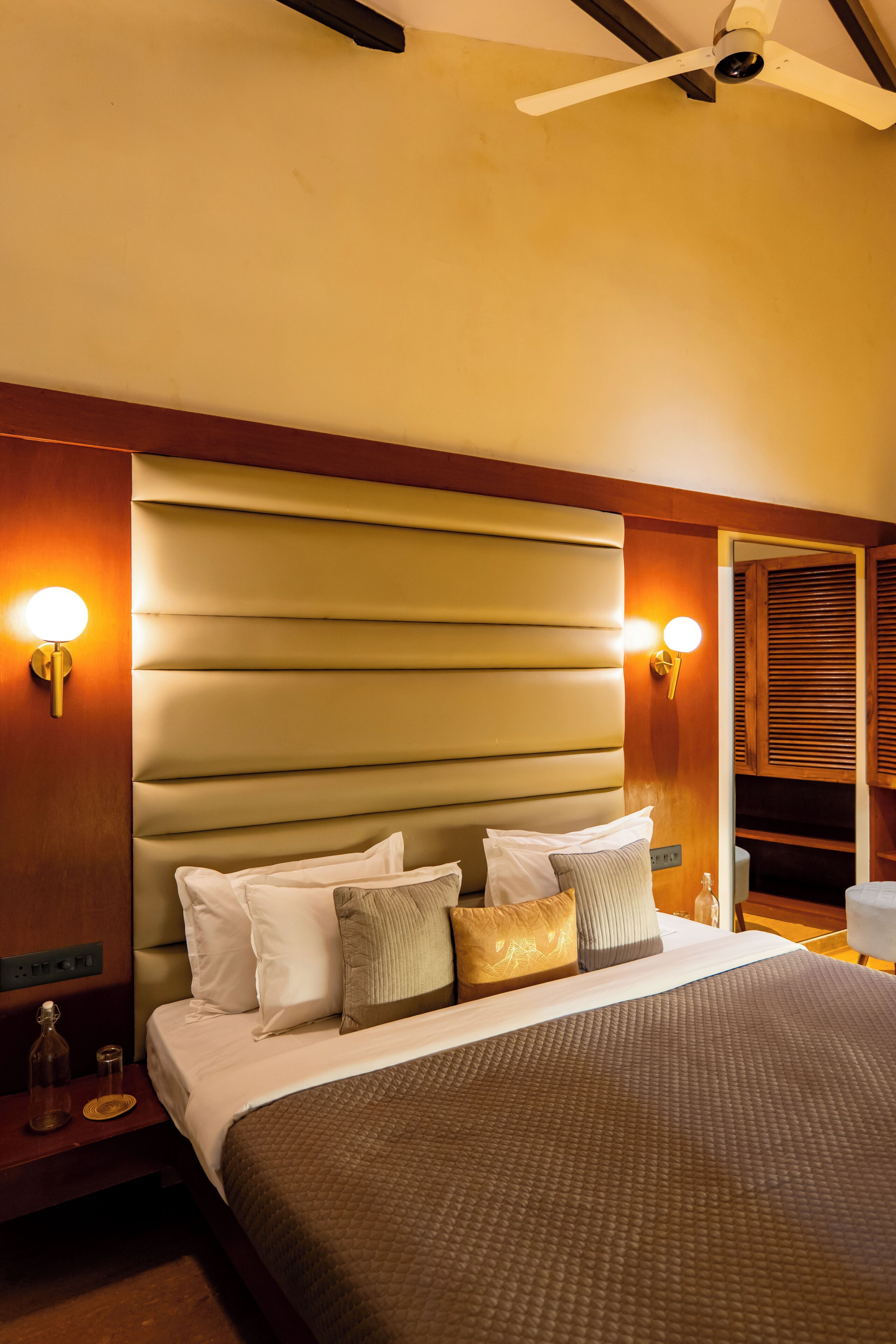 A hotel room with a large bed, headboard, bedside lamps, and a ceiling fan.